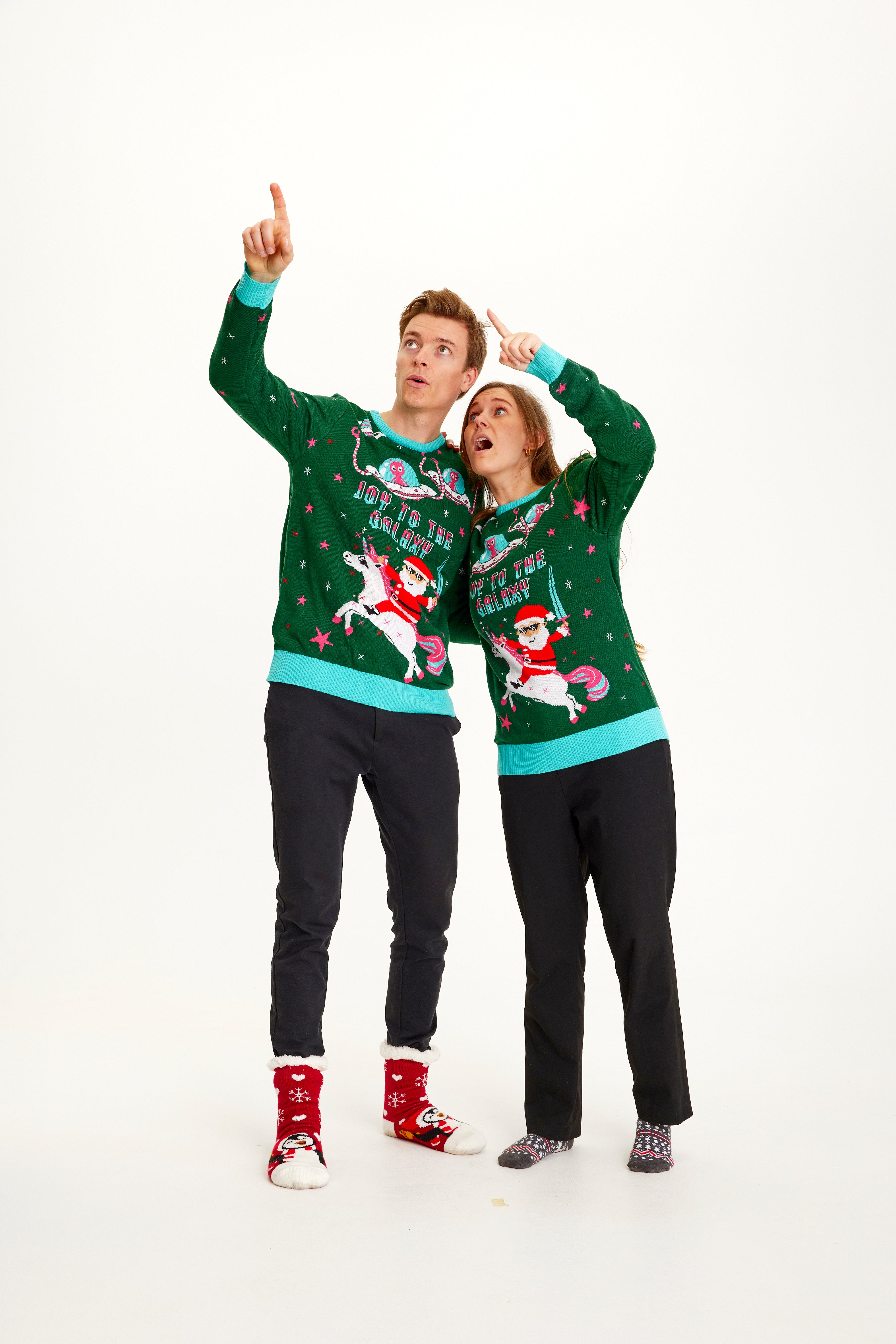 En mand og en kvinde kigger og peger til himlen og er begge iført en grøn julesweater.